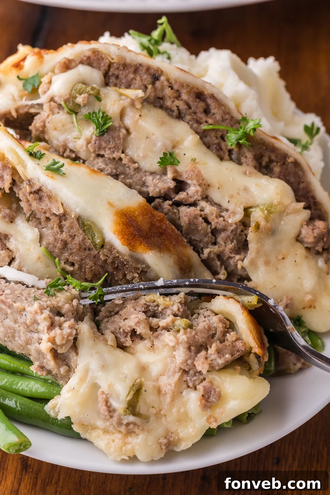 Up close shot of the Philly Cheesesteak Meatloaf sliced on a white serving plate with a fork taking out a bite