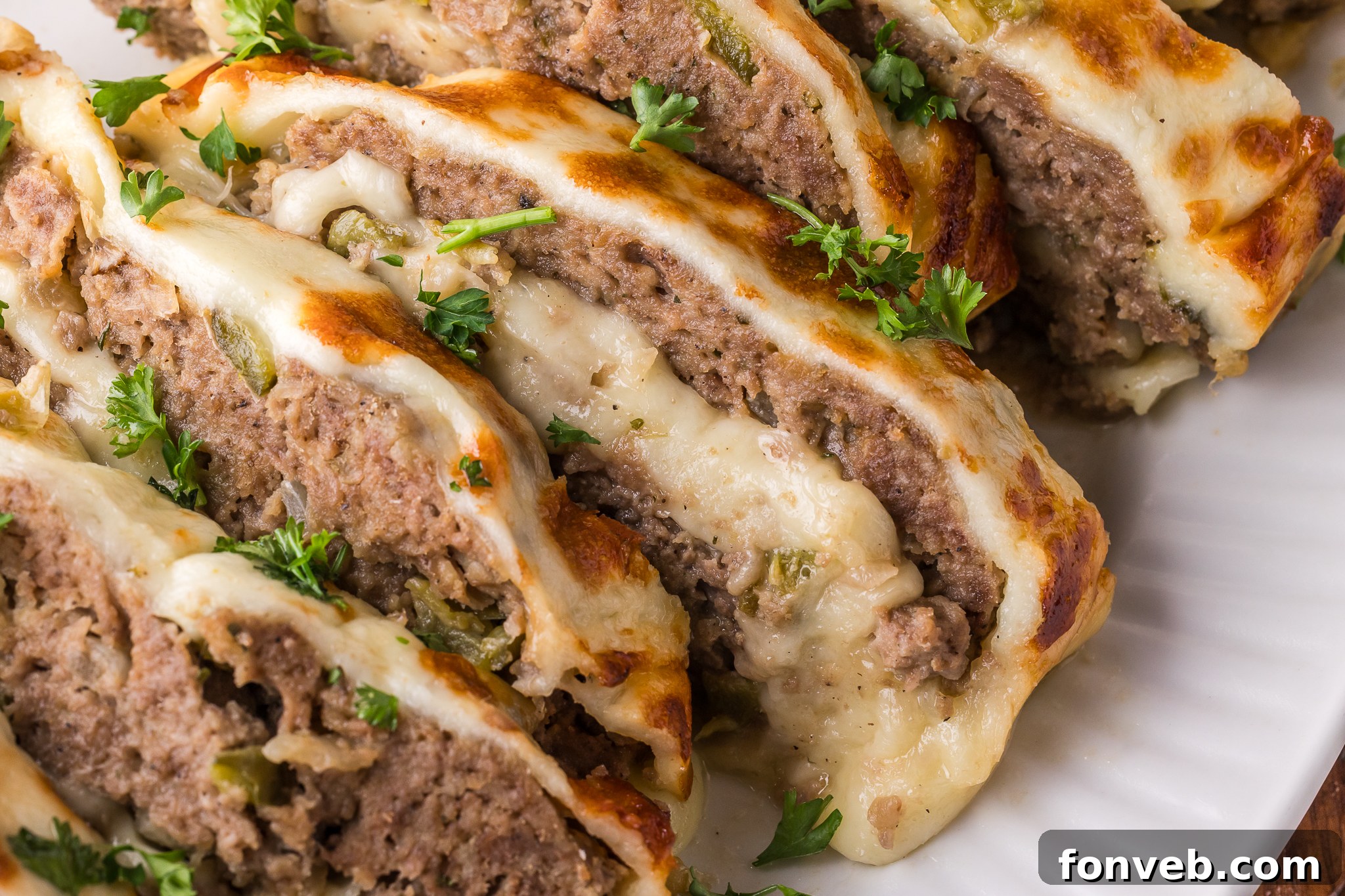 zoomed in shot of the Philly Cheesesteak Meatloaf sliced on a white serving plate showing the inside with melty cheese 