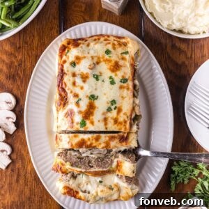 Stuffed Philly Cheesesteak Meatloaf on a white platter on wooden table that is partly sliced and ready to serve