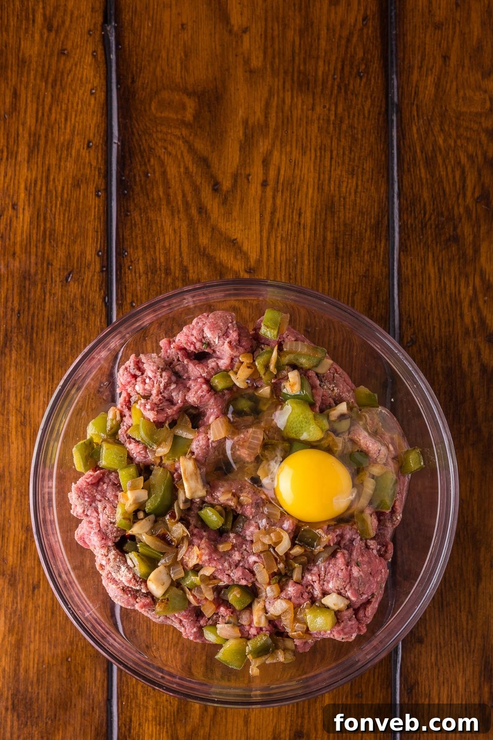 raw meat, with egg, and onions and peppers on a glass bowl on a wooden table