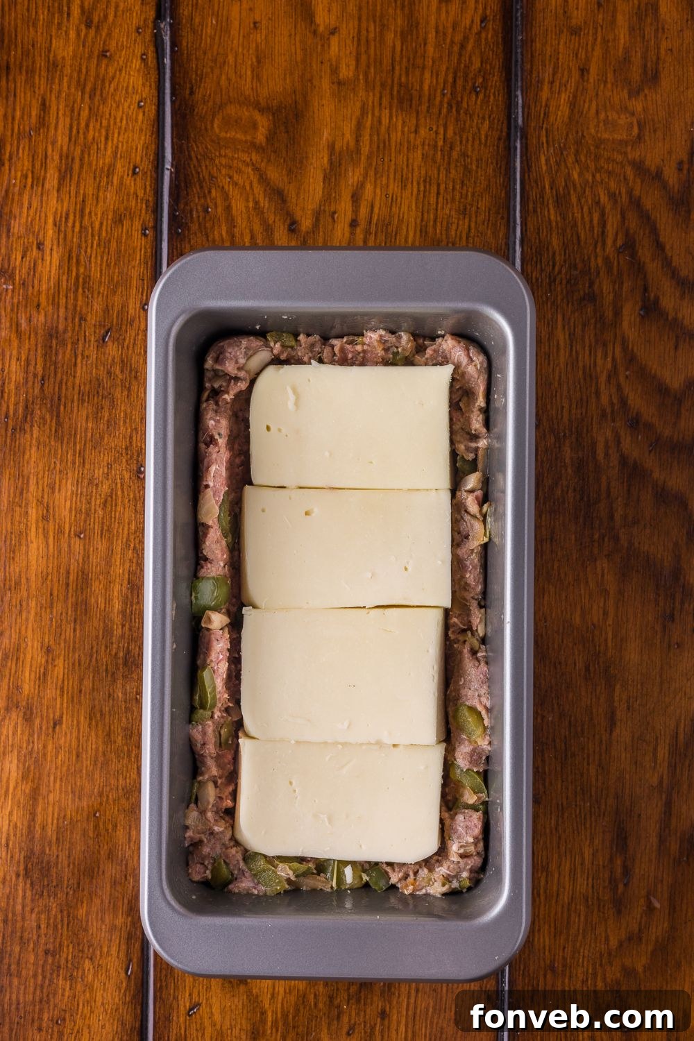 half of meat topped with provolone cheese in a loaf pan to make Stuffed Philly Cheesesteak Meatloaf