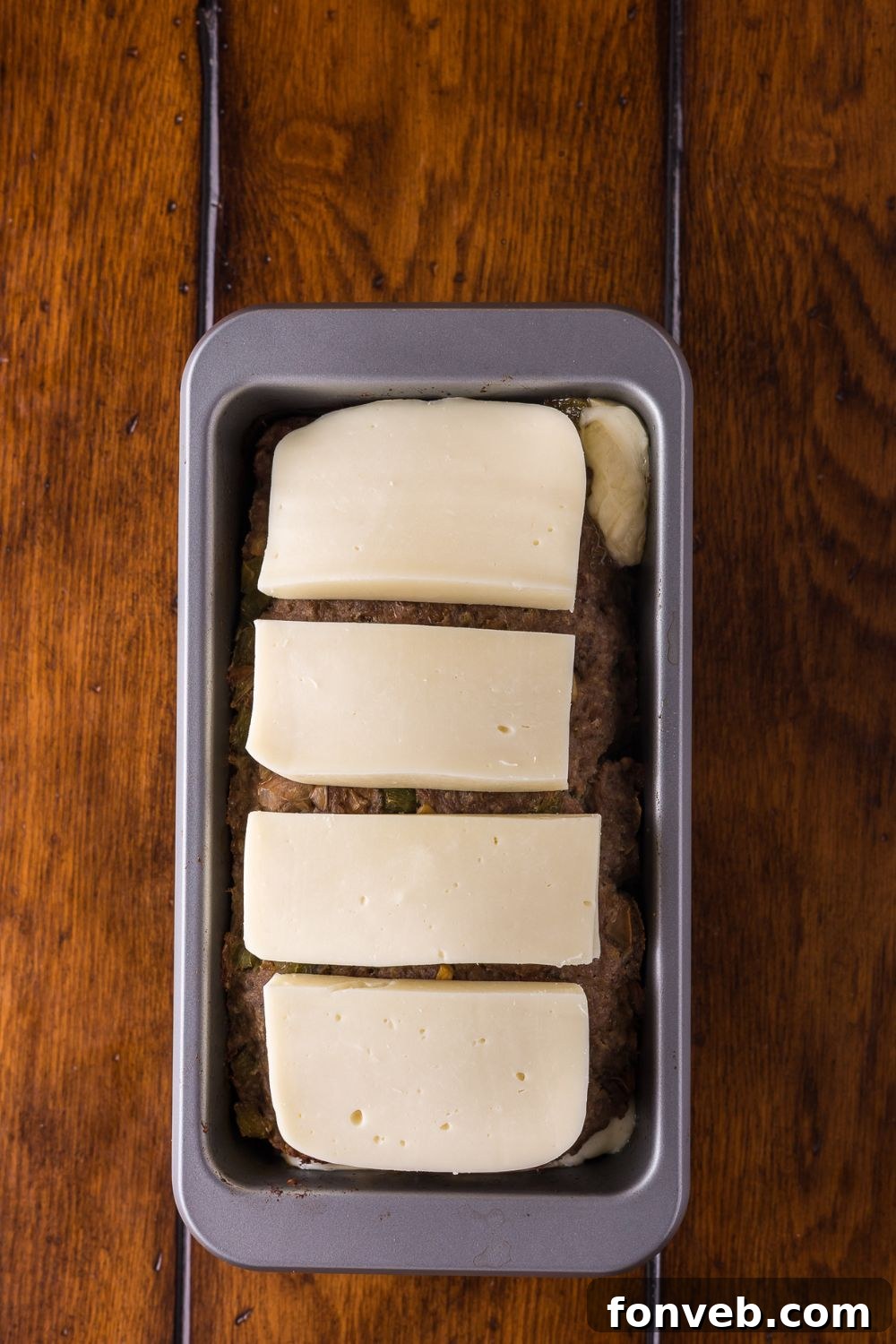 slices of provolone sitting on top of a raw Stuffed Philly Cheesesteak Meatloaf in loaf pan 