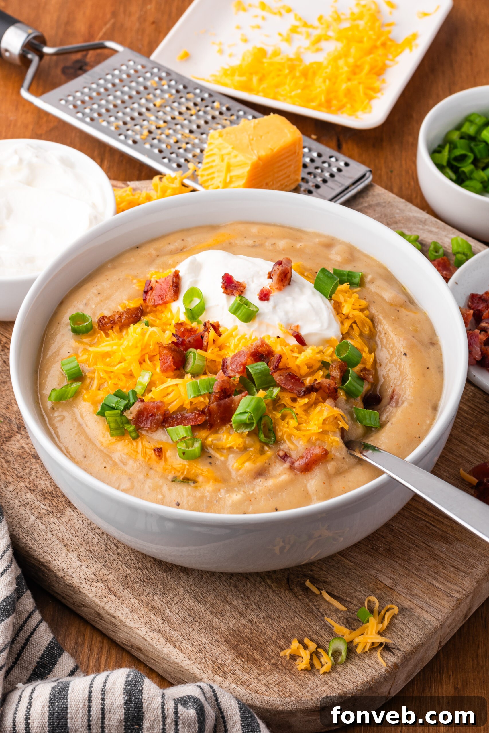 Crock pot loaded baked potato soup in a white bowl on a dark wood table with cheese grated in the background