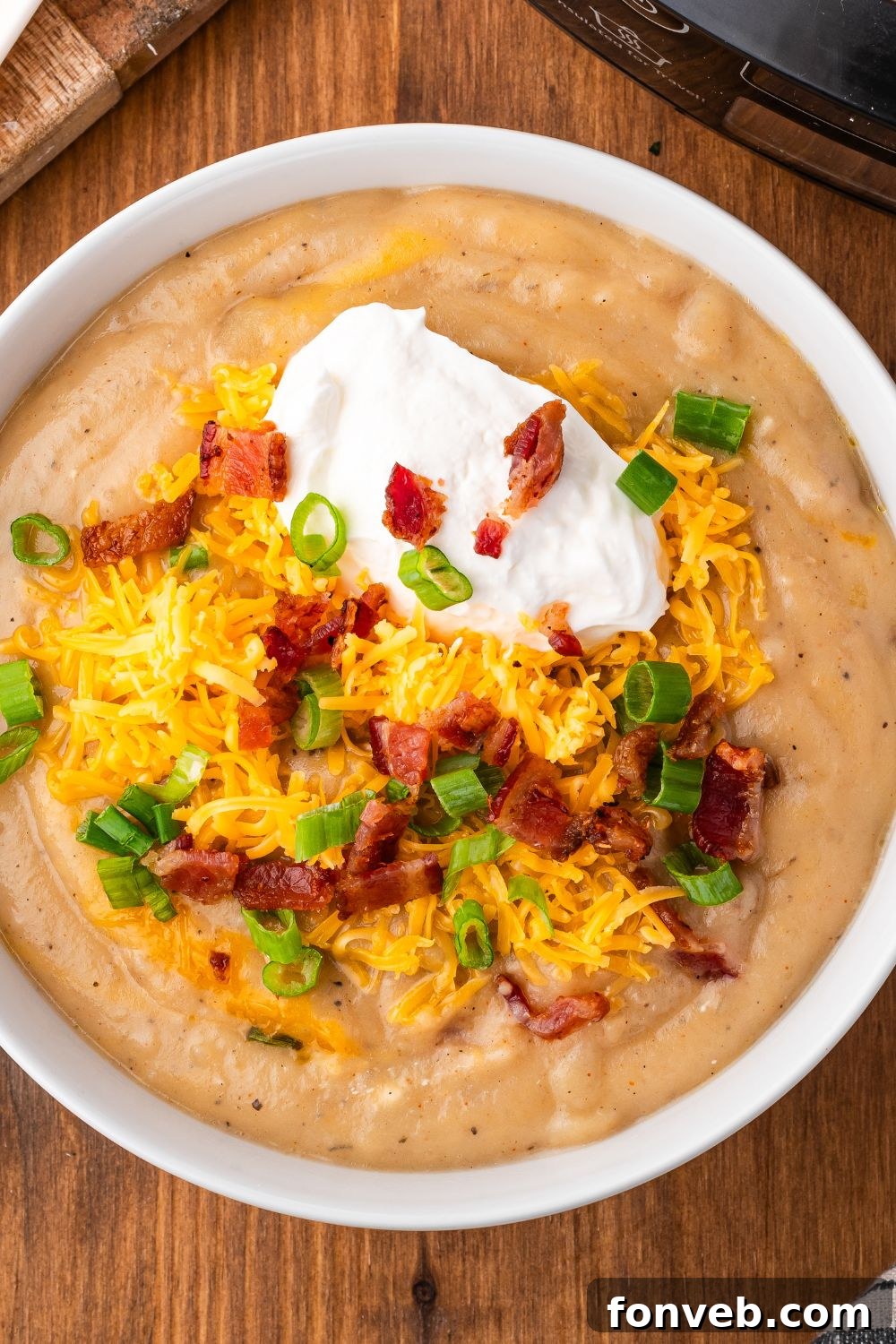 looking down at table with a white bowl full of Crockpot Loaded Baked Potato Soup and topped with crumbled bacons, shredded cheese, sour cream and more. 