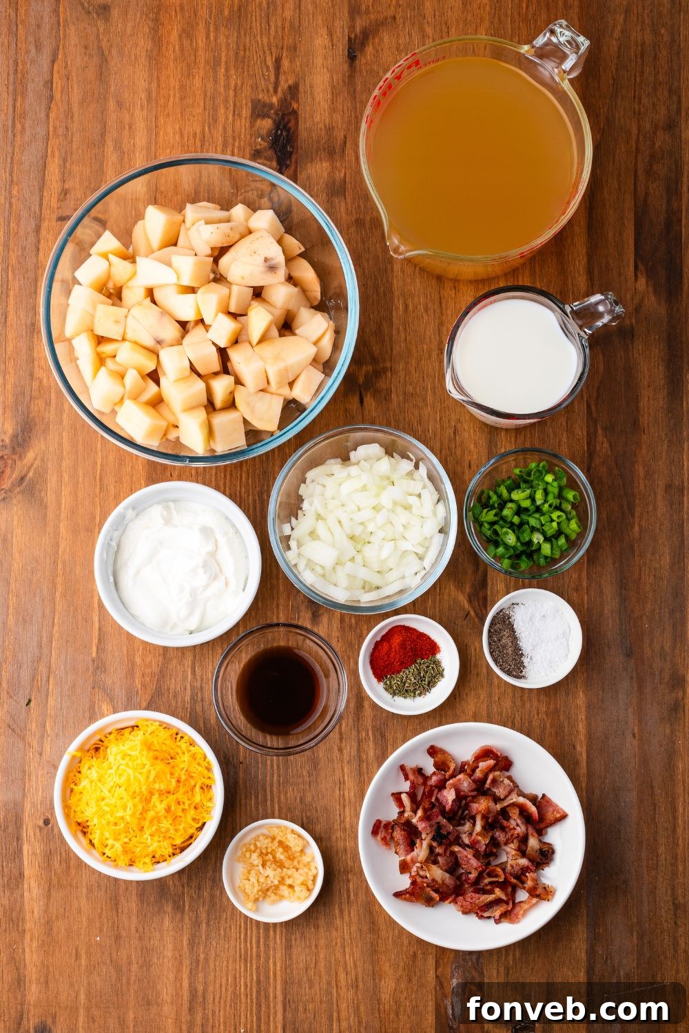 wooden table with all the ingredients in single serve bowls for making Crockpot Loaded Baked Potato Soup. Potatoes, bacon, onions, cheese, and all the other ingredients. 