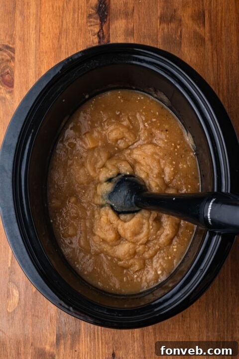 immersion blender in a black crockpot on wooden table mixing up the potato soup to make it thicker and creamy