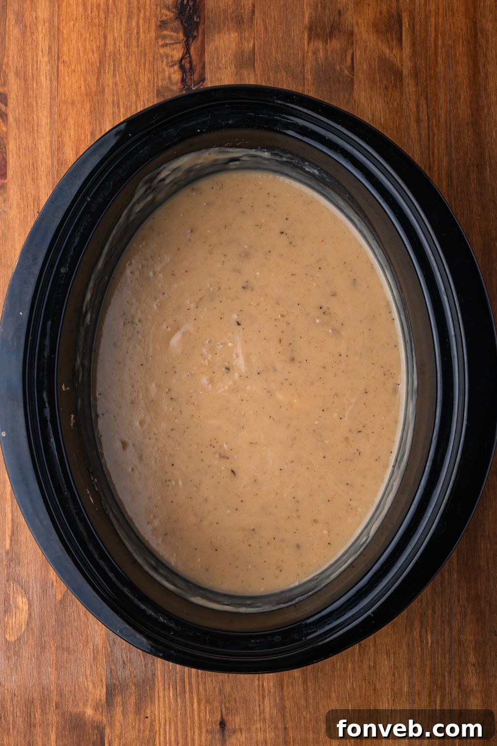 creamy Crockpot Loaded Baked Potato Soup sitting in a black crockpot sitting on a wooden table 
