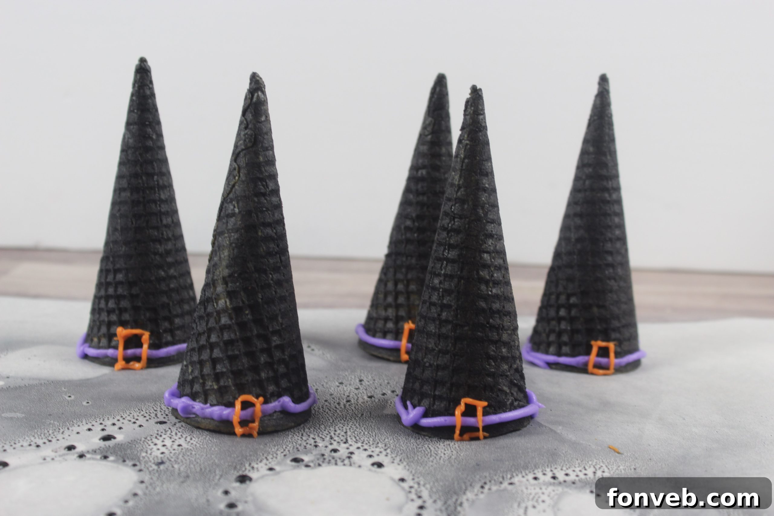 Wicked Witch Hat Cupcakes 10 Hands carefully piping purple and orange icing details onto a black sugar cone witch hat.