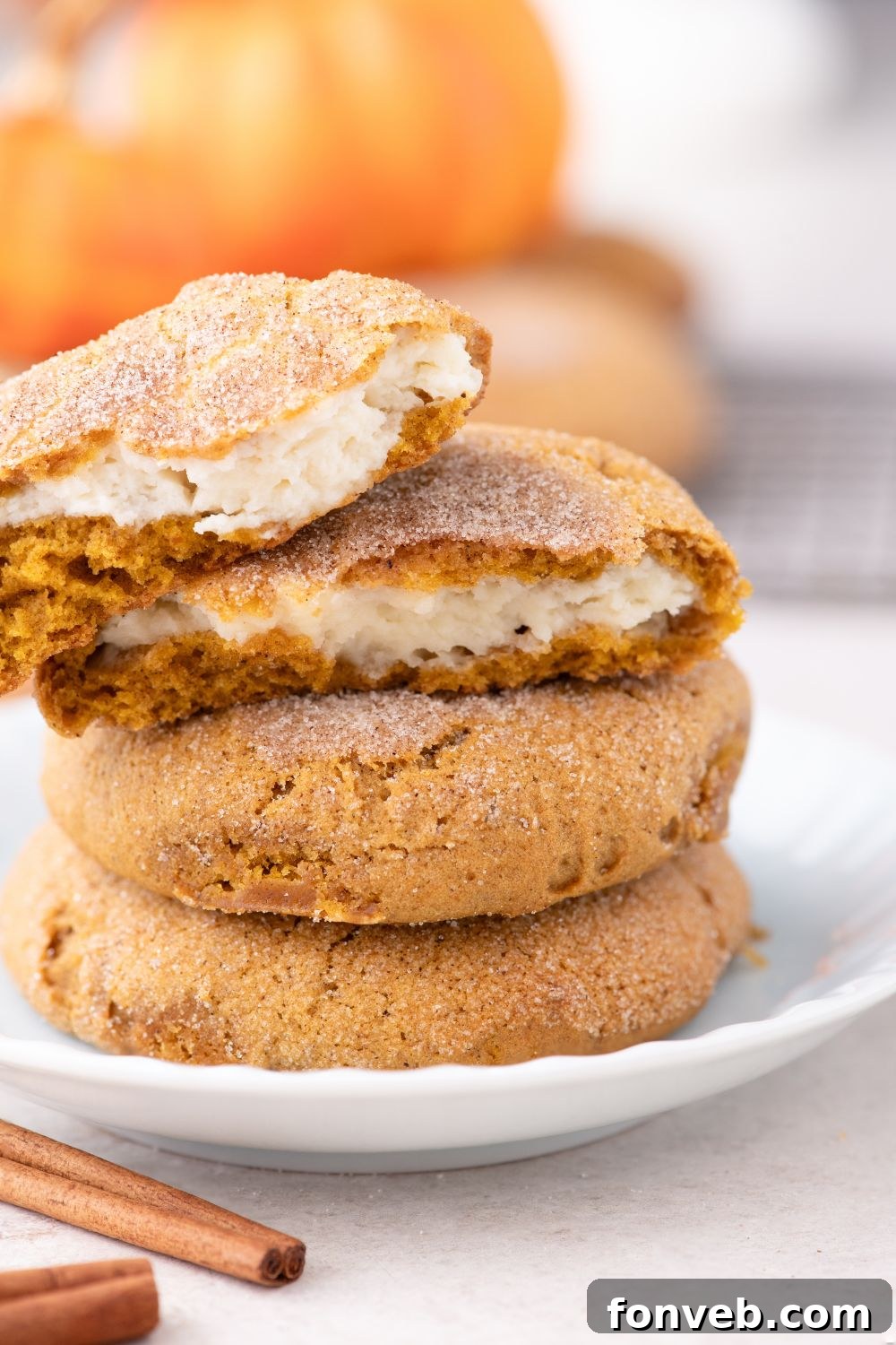 white plate with a stack of Pumpkin Cheesecake Cookies on table with one cookie cut in half