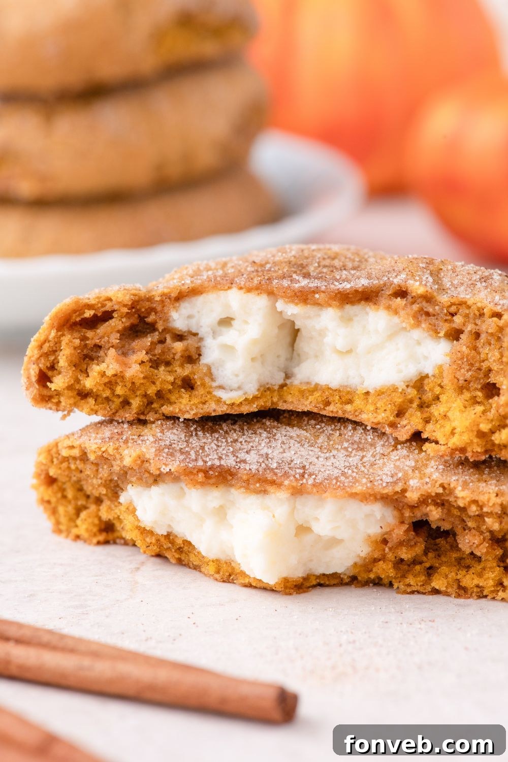 white table with two pumpkin cheesecake cookies on it, with a cinnamon stick placed in frotn 