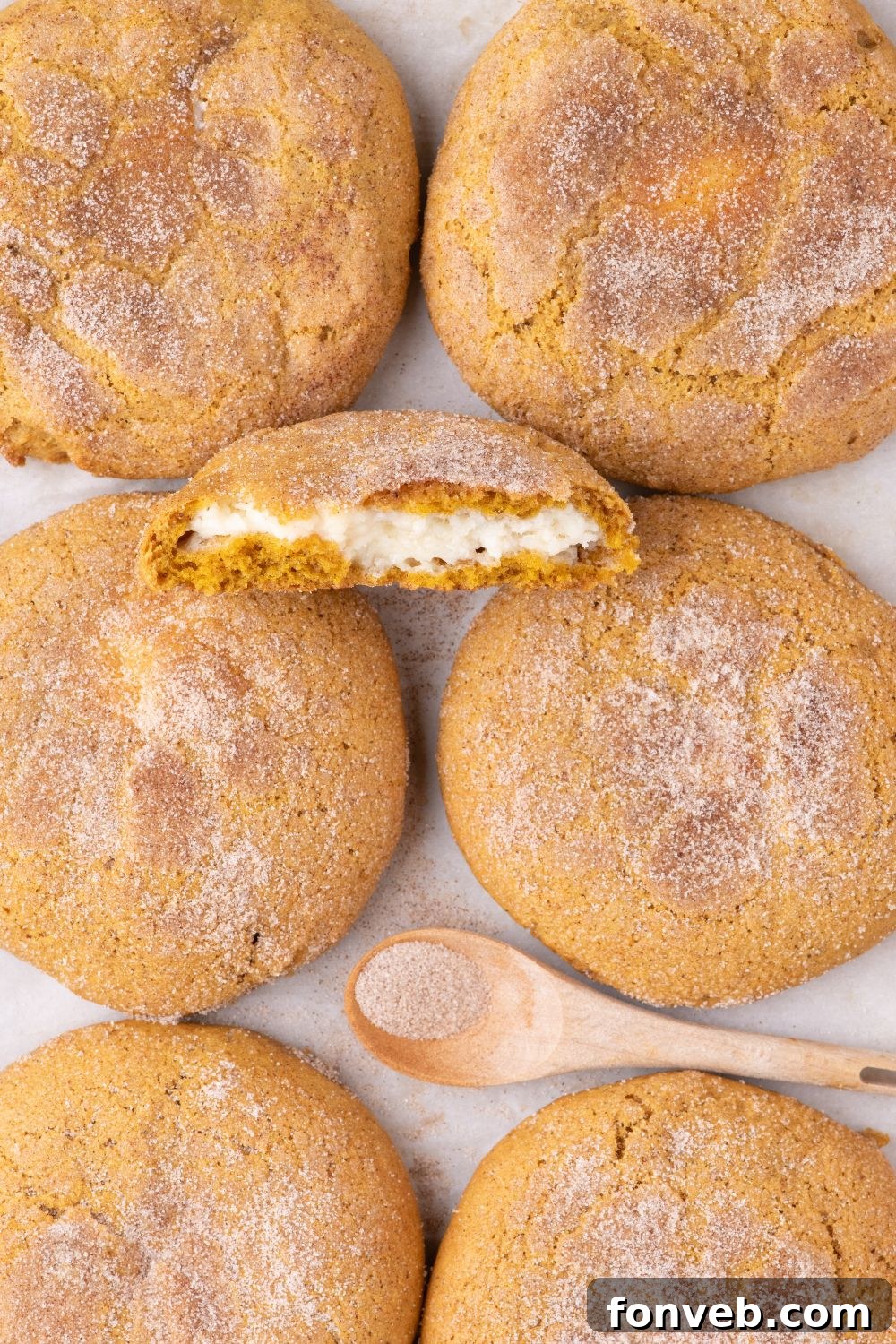 Pumpkin Cheesecake Cookies placed on table with one cookie cut in half and a spoon of cinnamon and sugar