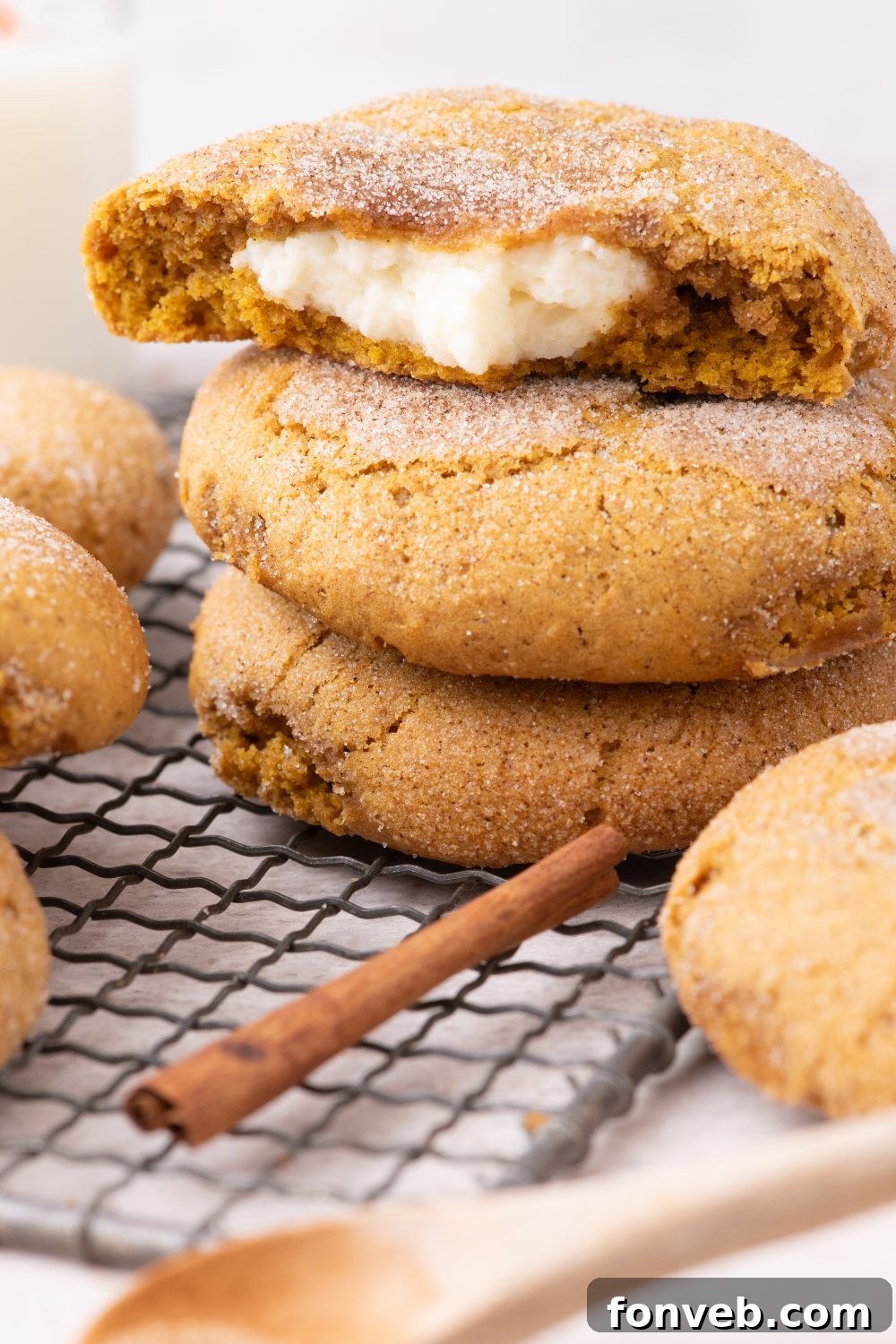 Pumpkin Cheesecake Cookies stacked on a cooling rack on table with a cinnamon stick and wooden spoon  in front 