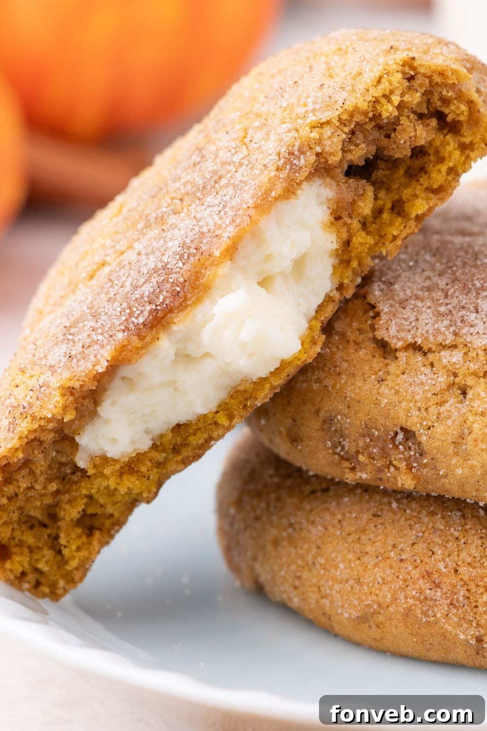 2 Pumpkin Cheesecake Cookies on a white plate with one cookie with some bites out of it to show the cheesecake filling 
