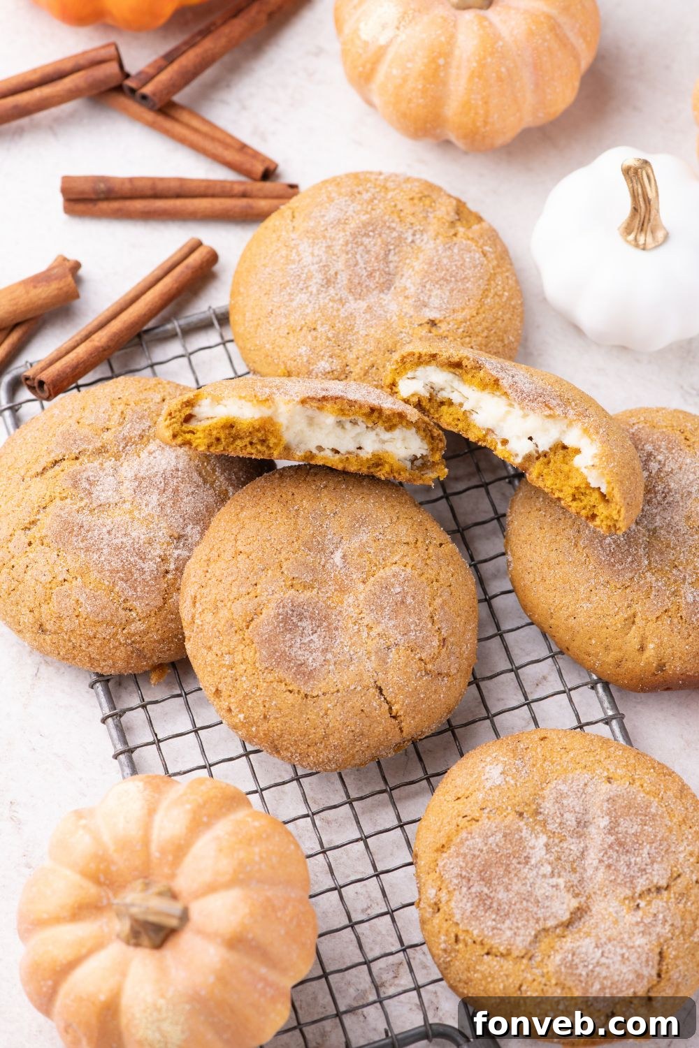 Pumpkin Cheesecake Cookies on a cooling rack on a white table with cinnamon sticks and pumpkins around 