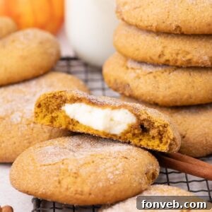 Pumpkin Cheesecake Cookies stacked on a cooling rack on table with one cookie cut in half to show the filling