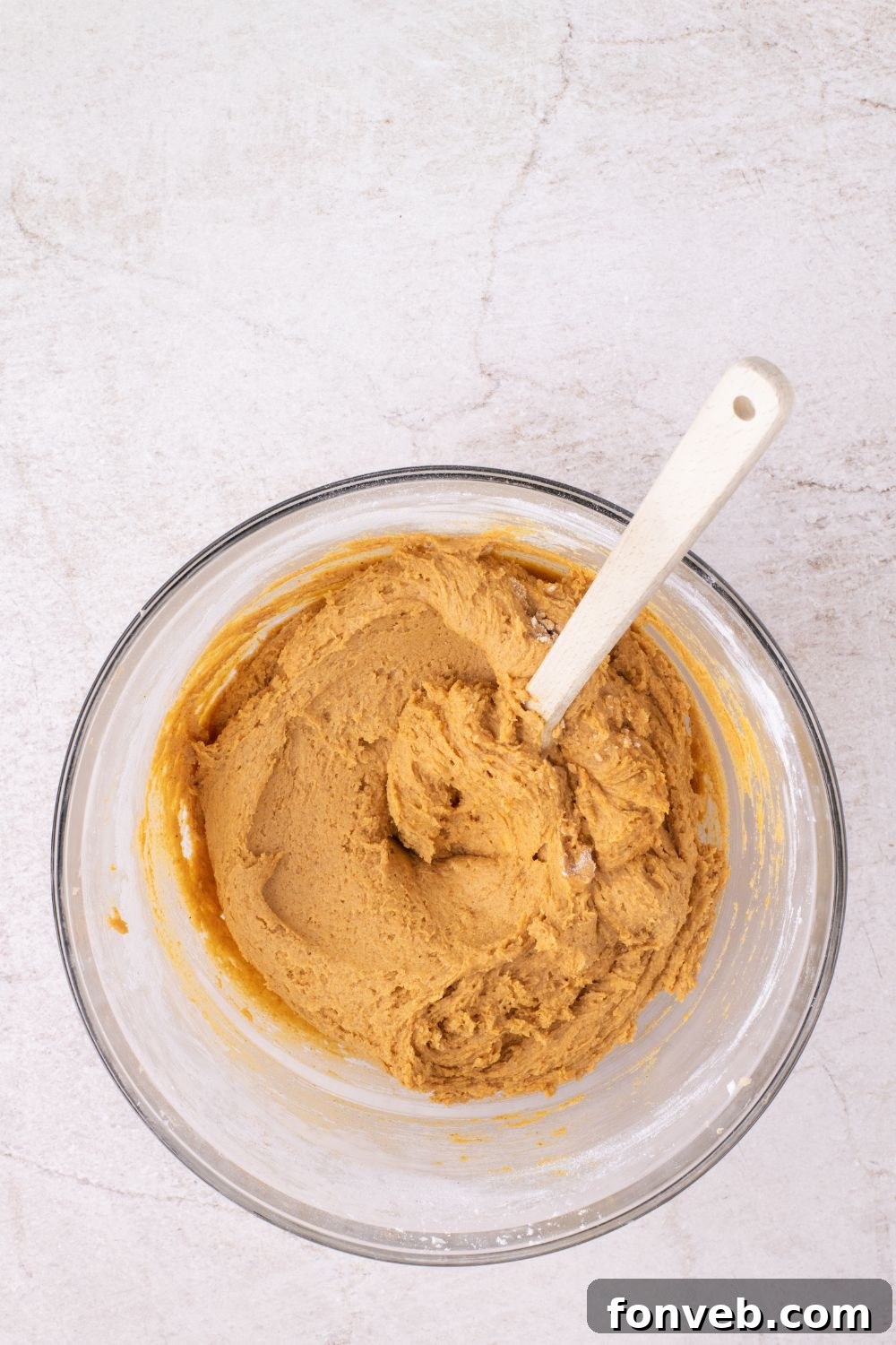 pumpkin cookie batter in a glass bowl with a spatula on table 