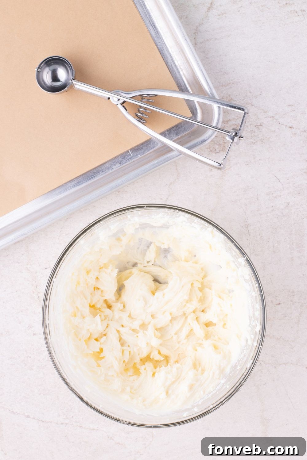 cheesecake batter in a glass bowl with a cookie sheet to side and cookie scoop