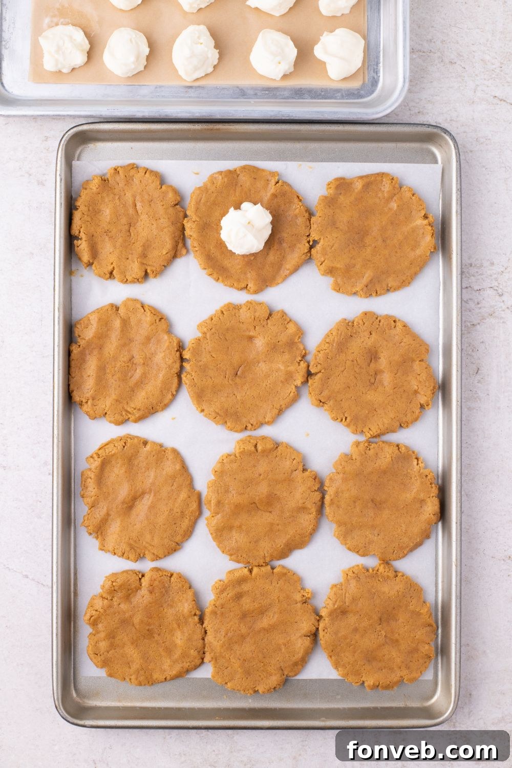 flat raw cookie dough on baking tray for cookies with a cheesecake batter in center of one of the cookies 