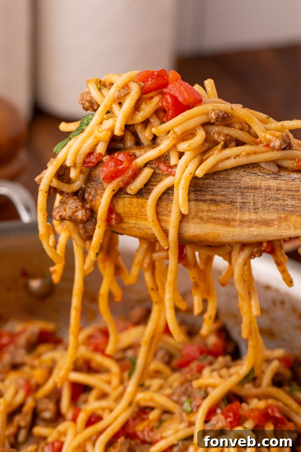 One Pot Cheesy Taco Spaghetti 12 wooden tongs with a bunch of taco spaghetti being lifted out of skillet