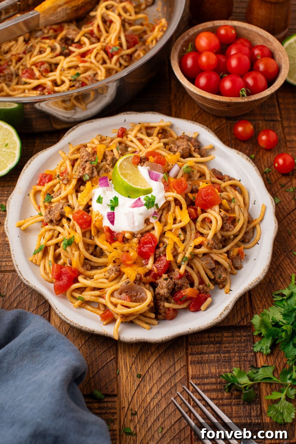 One Pot Cheesy Taco Spaghetti 15 A plate with a pile of pasta with tomatoes, sour cream, a lime wedge on top, and more then a small tomatoes in a bowl with cilantro