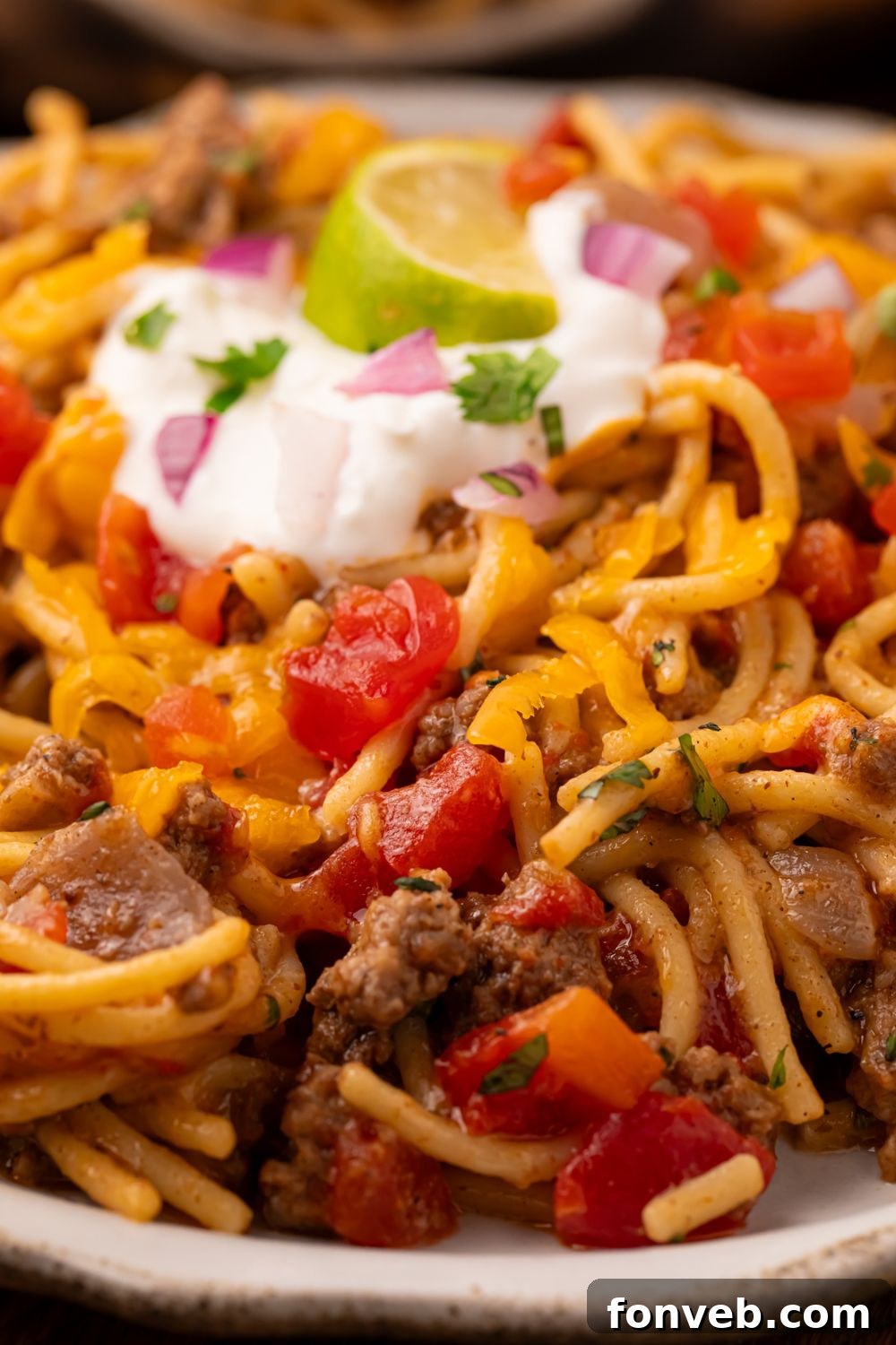 One Pot Cheesy Taco Spaghetti 17 Taco spaghetti skillet on a white plate with a dollop of sour cream in center, cilantro, and a lime wedge