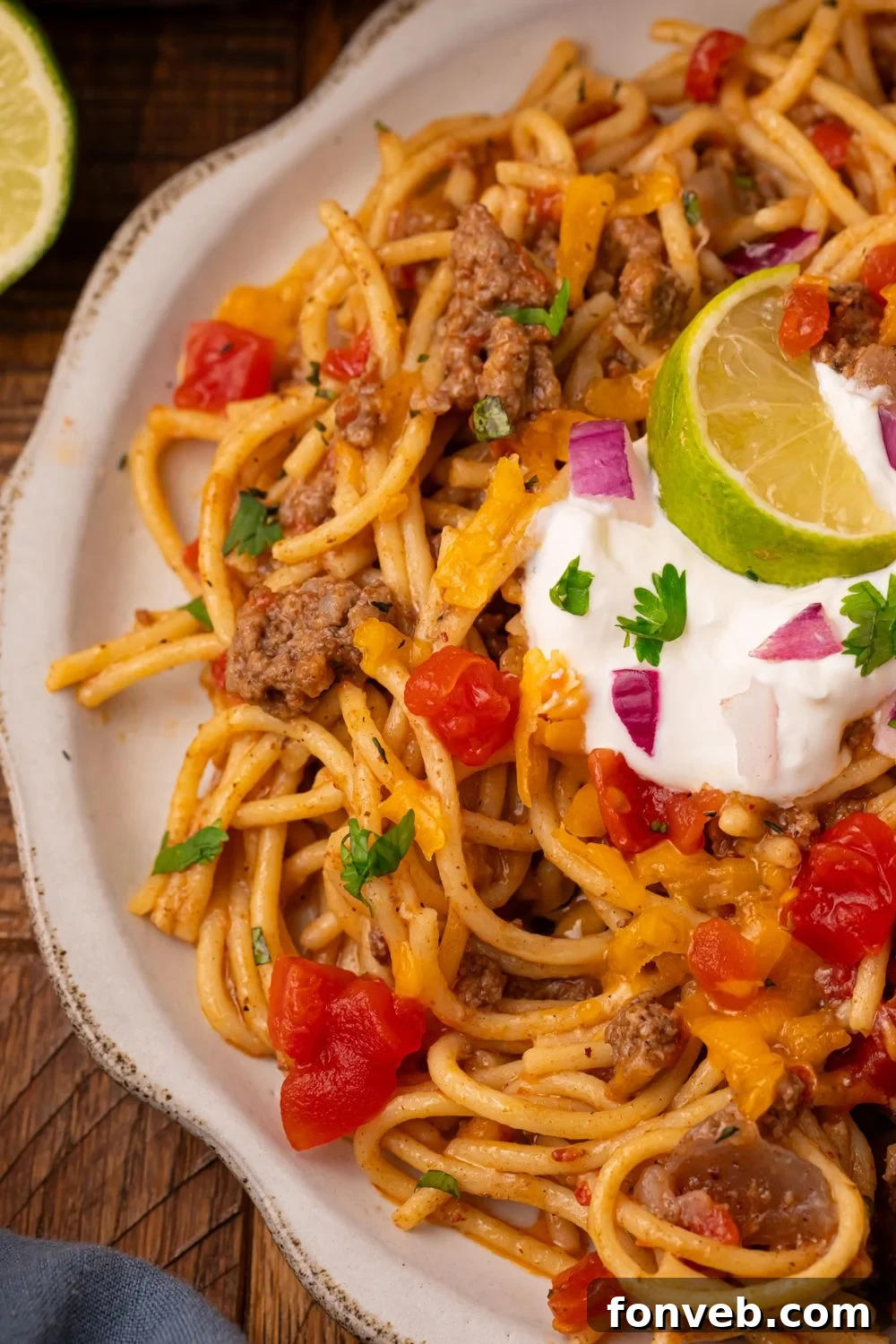 One Pot Cheesy Taco Spaghetti 19 view of half a plate on wooden table with a full plate of Cheesy Taco Spaghetti on it