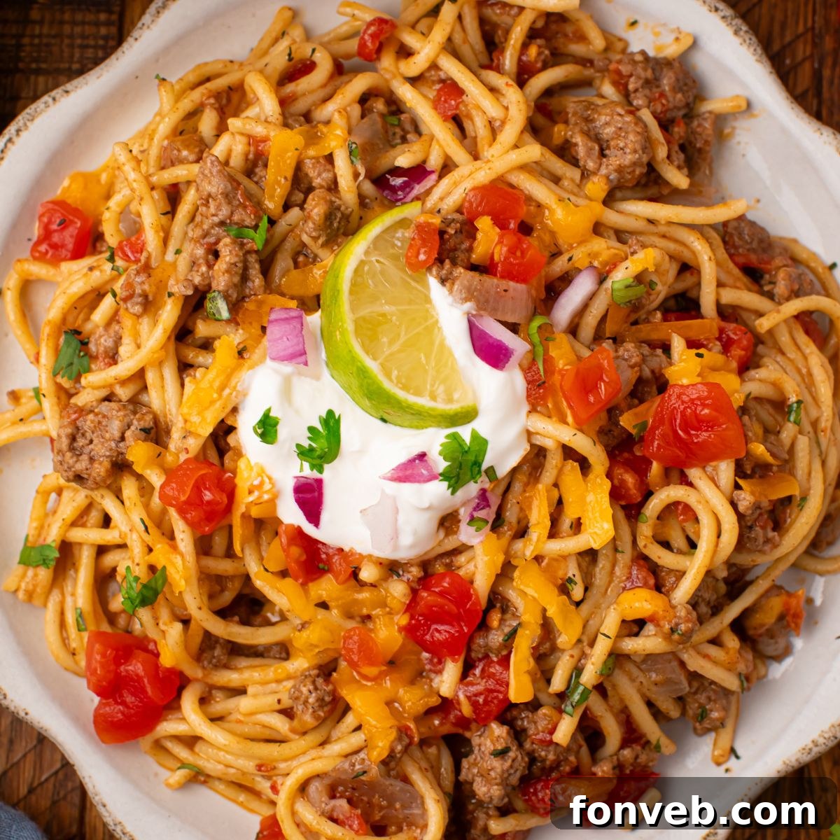 One Pot Cheesy Taco Spaghetti 3 white plate on wooden table that is piled full of Cheesy Taco Spaghetti with sour cream and lime wedge on top of mixture