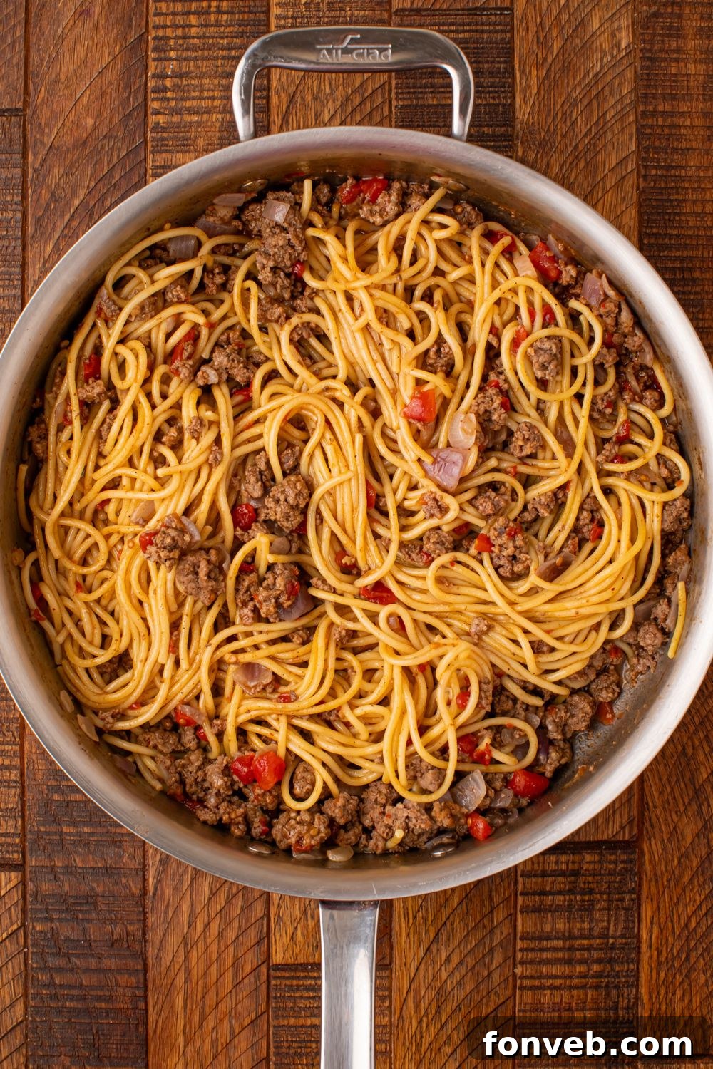 One Pot Cheesy Taco Spaghetti 8 a skillet on wooden table with ground beef, veggies and pasta inside being mixed up