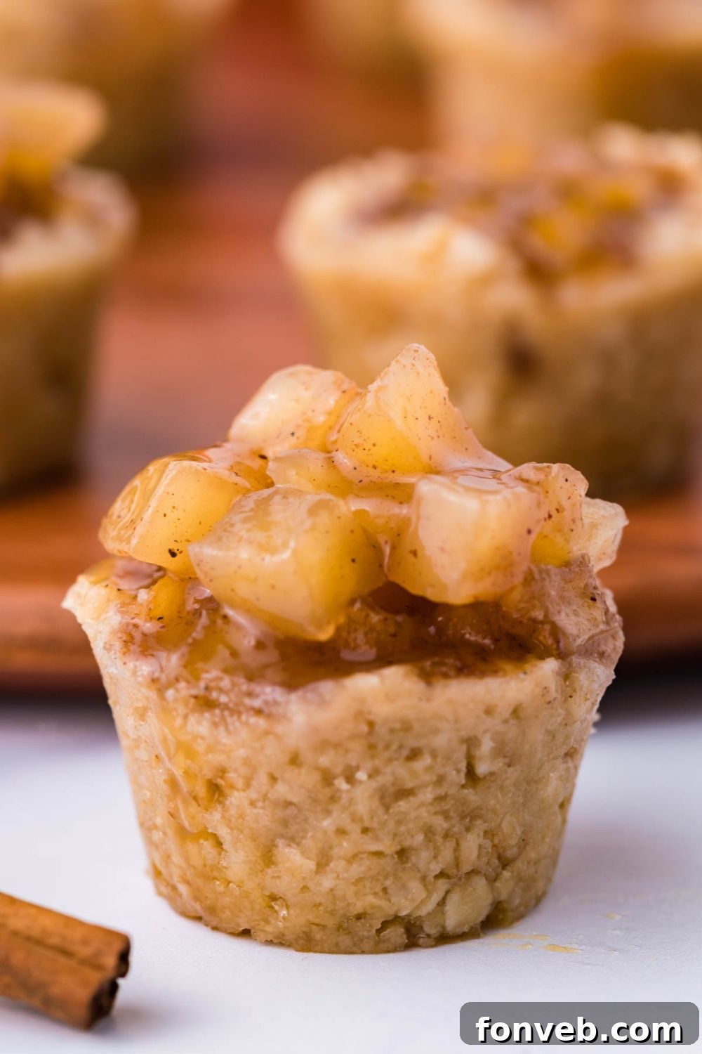 close up look of a Mini Apple Crisp Bites on white table with a cinnamon stick in front, and more bite cups behind it on a wooden tray
