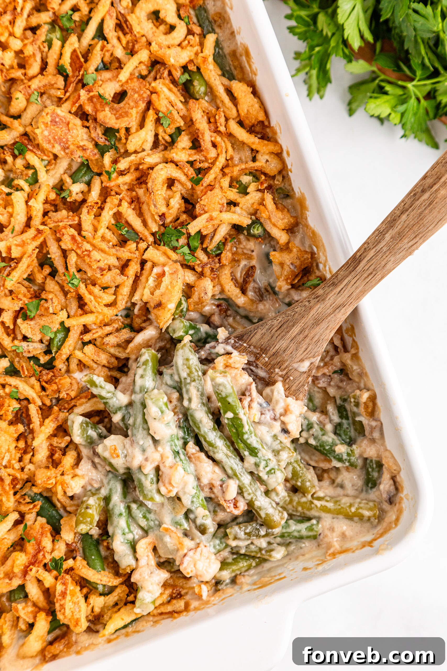 Best Ever Green Bean Casserole in a white baking dish with a spoon scooping some out 