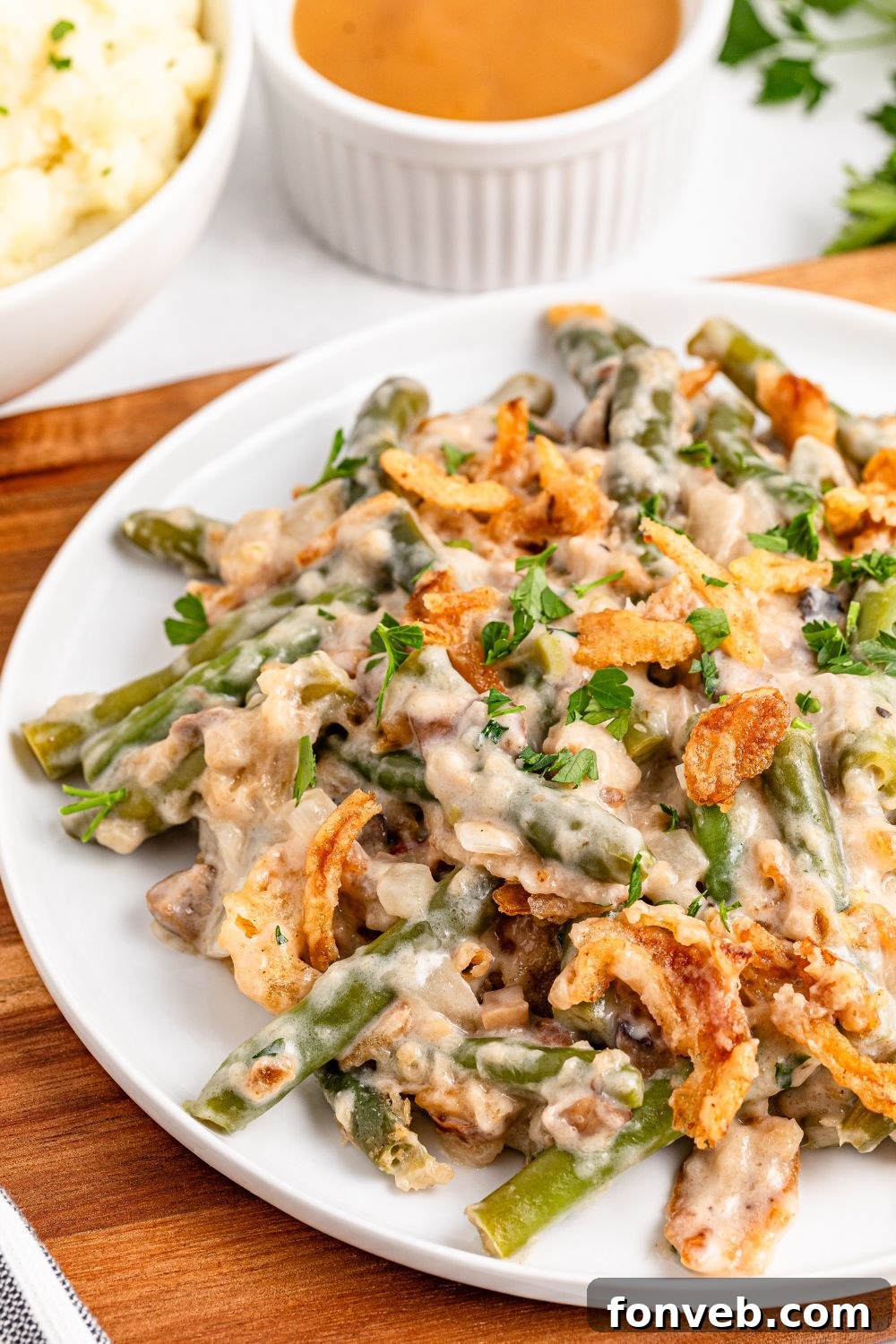 white plate sitting on table full of Green Bean Casserole. A brown towel is under the plate on table 