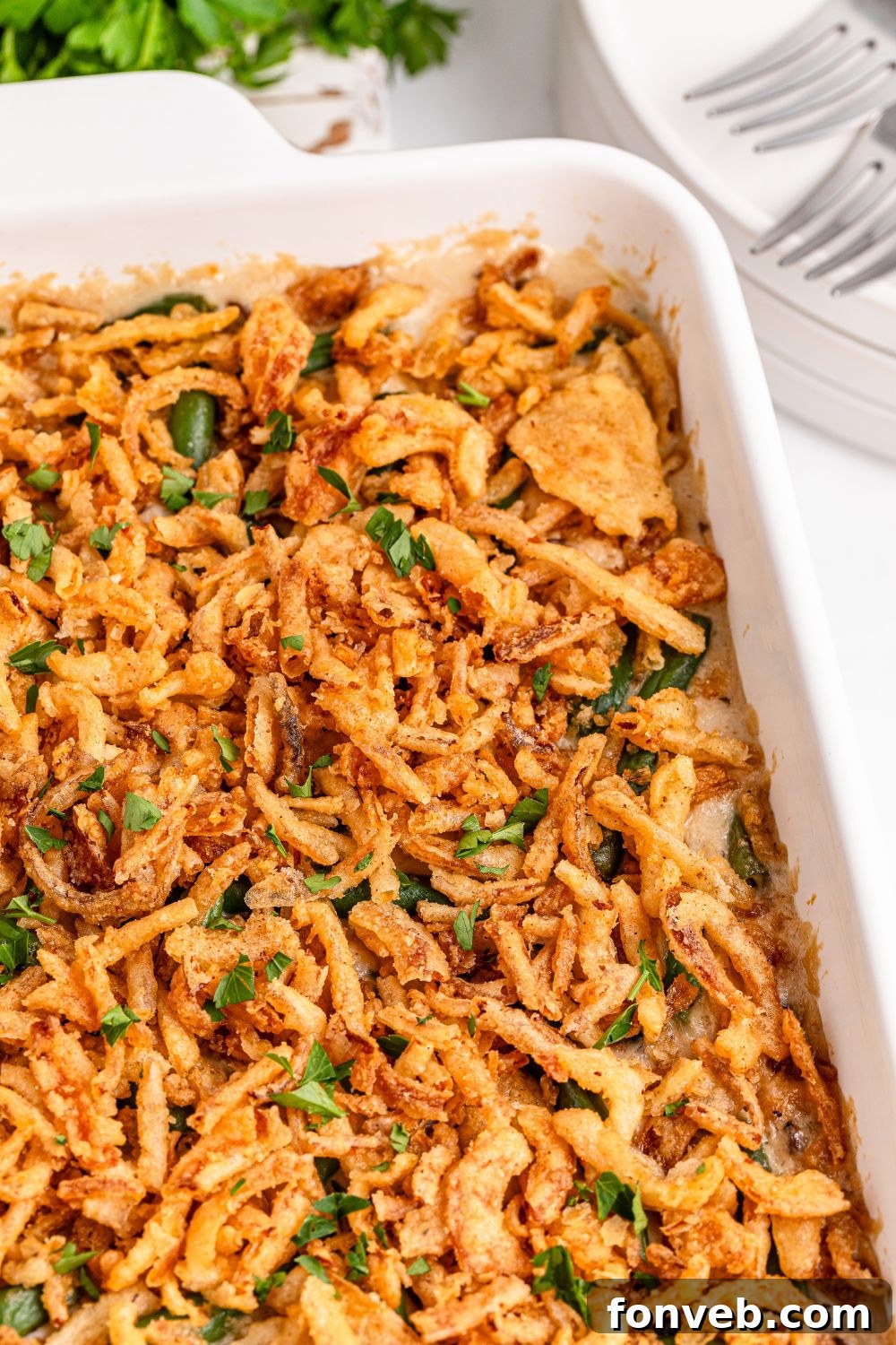 Green Bean Casserole in a white pan on table with plates and fork to side 