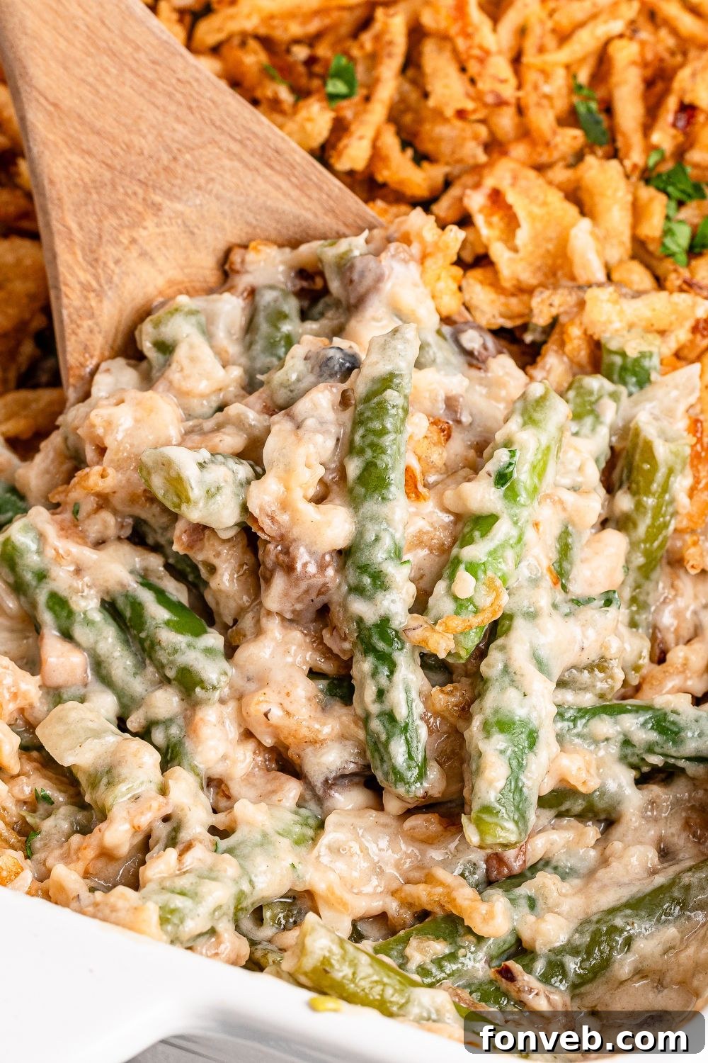 wooden spoon scooping up some of the Green Bean Casserole in a white baking dish on table 