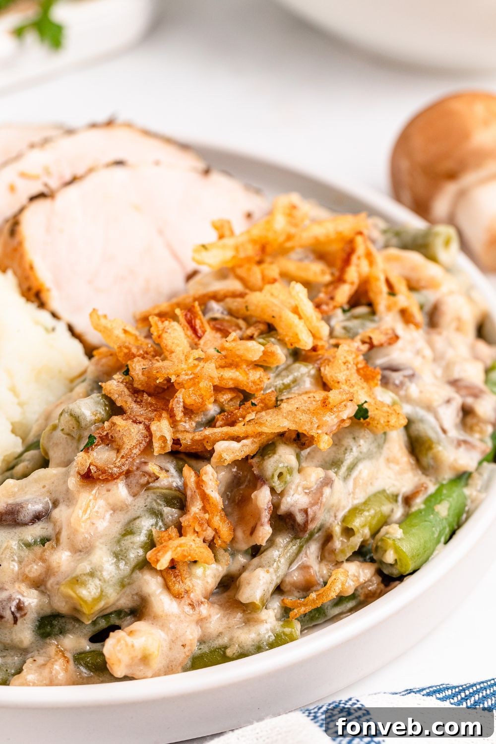 Green Bean Casserole on a round plate with some sliced turkey behind it on table and a striped towel in front of plate 