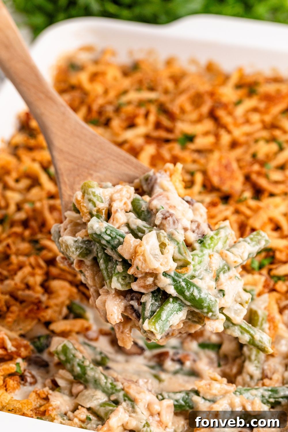 white rectangle pan on table full of Green Bean Casserole with a wooden spoon scooping some out of pan 