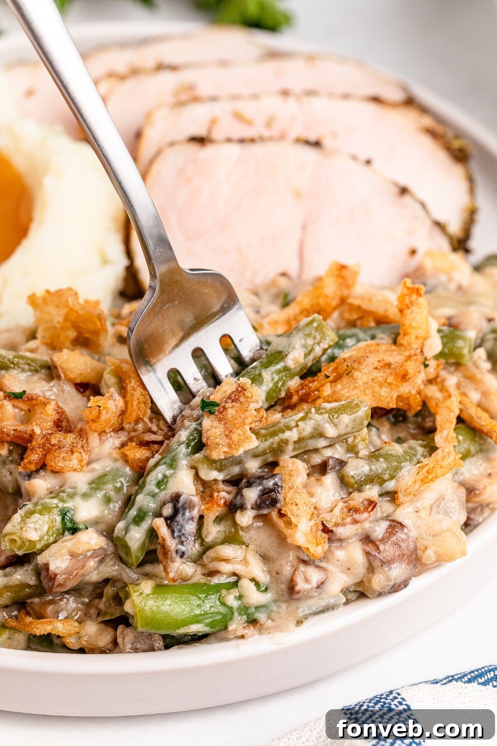 forking poking into plate full of Green Bean Casserole, with sliced turkey breast behind it and a bit of mashed potatoes and gravy