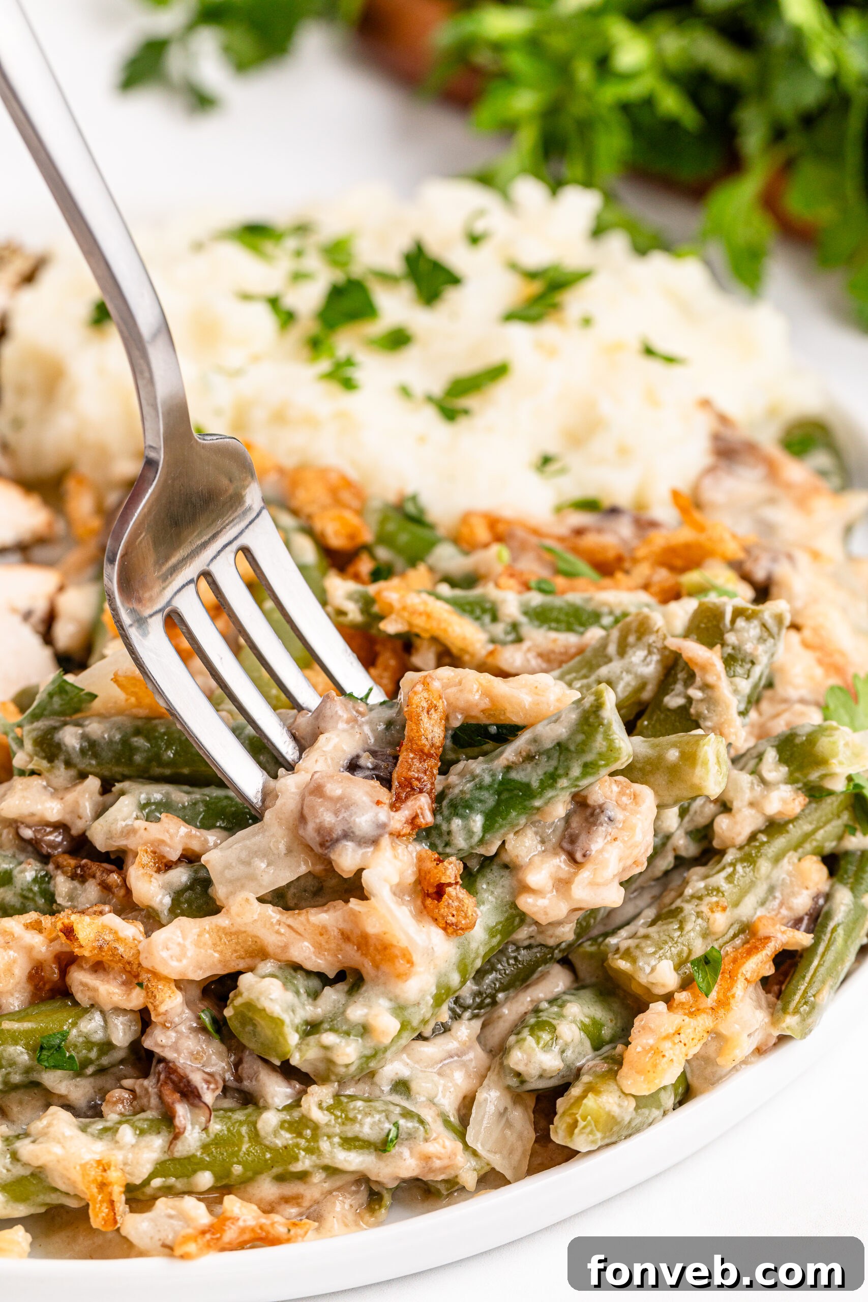 a fork going in for a bite of the Best Ever Green Bean Casserole in a white plate