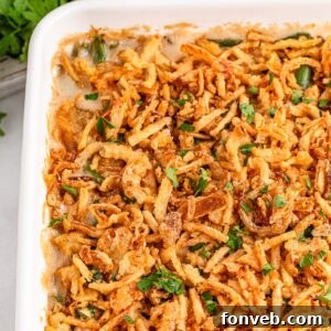 Green Bean Casserole in a white casserole dish sitting on table with fresh parsley sprinkled on top of casserole