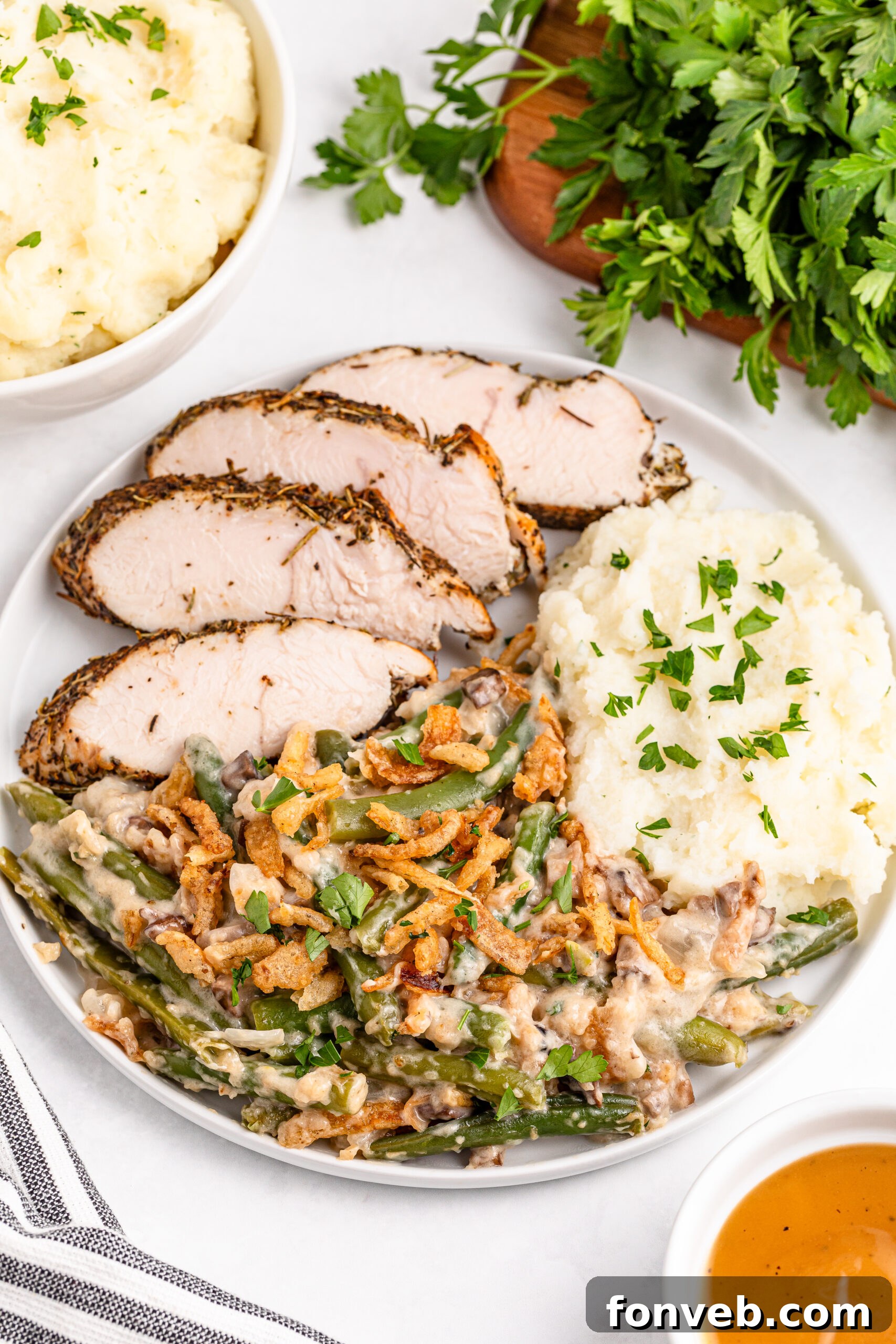 Green Bean Casserole on a white plate along side mashed potatoes and sliced turkey 