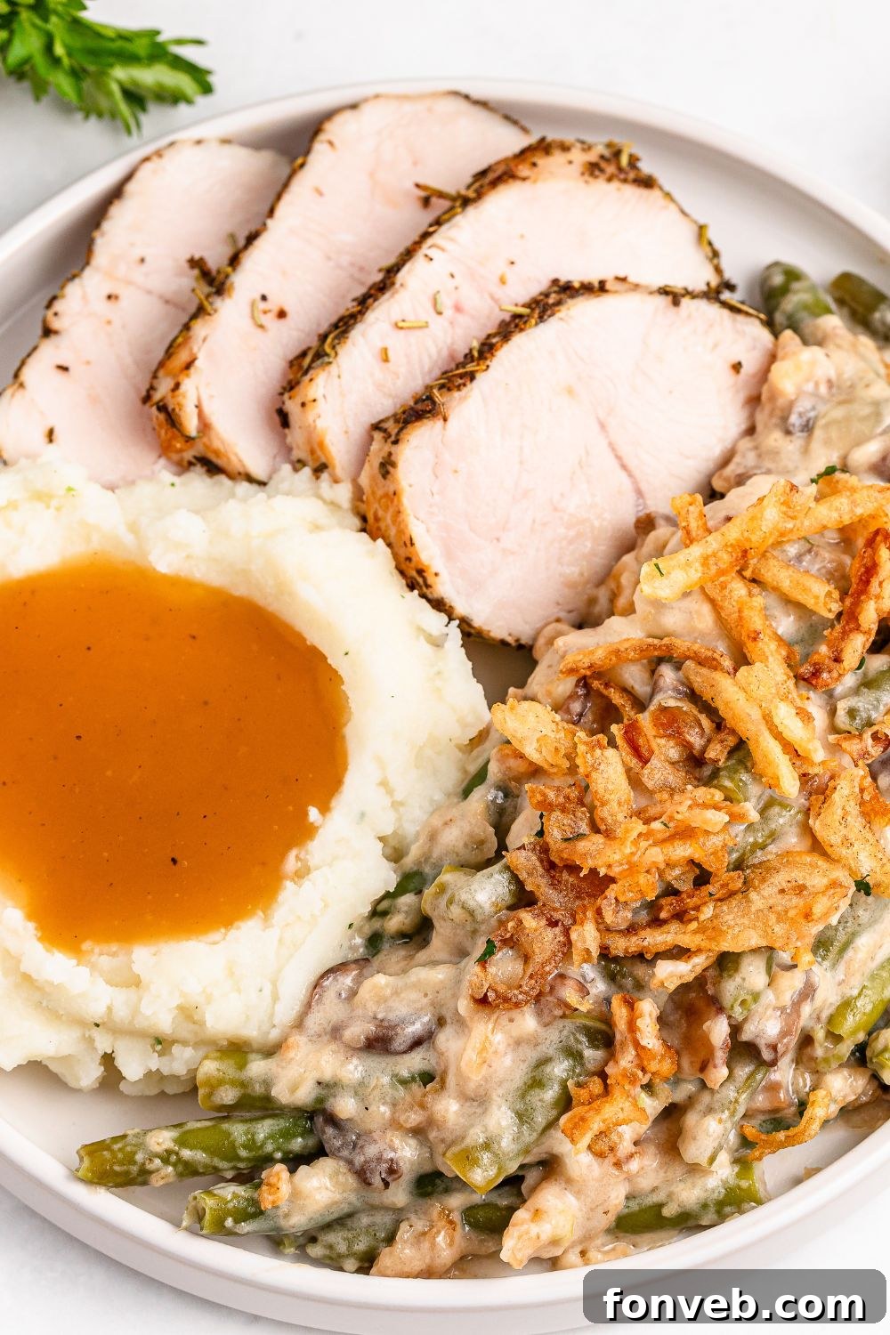 a white plate on a table with slices of turkey, scoop of mashed potatoes and gravy and some green bean casserole on it 