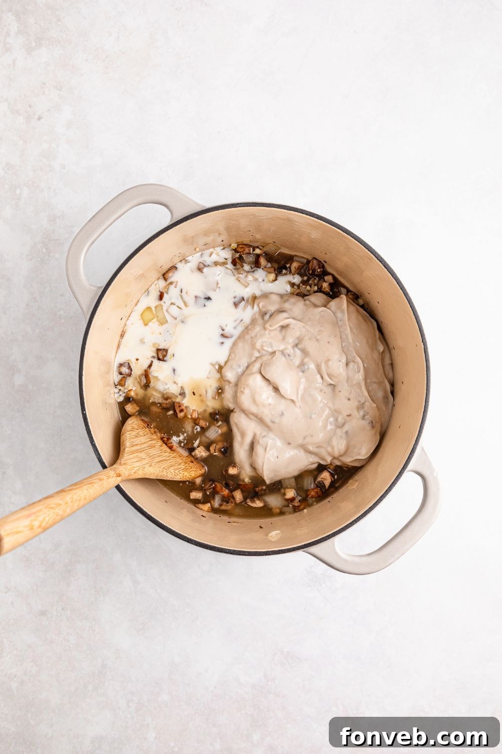 cream colored saucepan on table full of cooked veggies, cream soup and milk with wooden spoon 