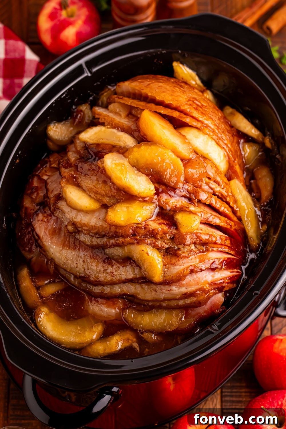 Tender and Juicy Slow Cooker Apple Glazed Ham 16 looking down at wooden table with a black slow cooker with apple glazed spiral ham. Fresh apples around table