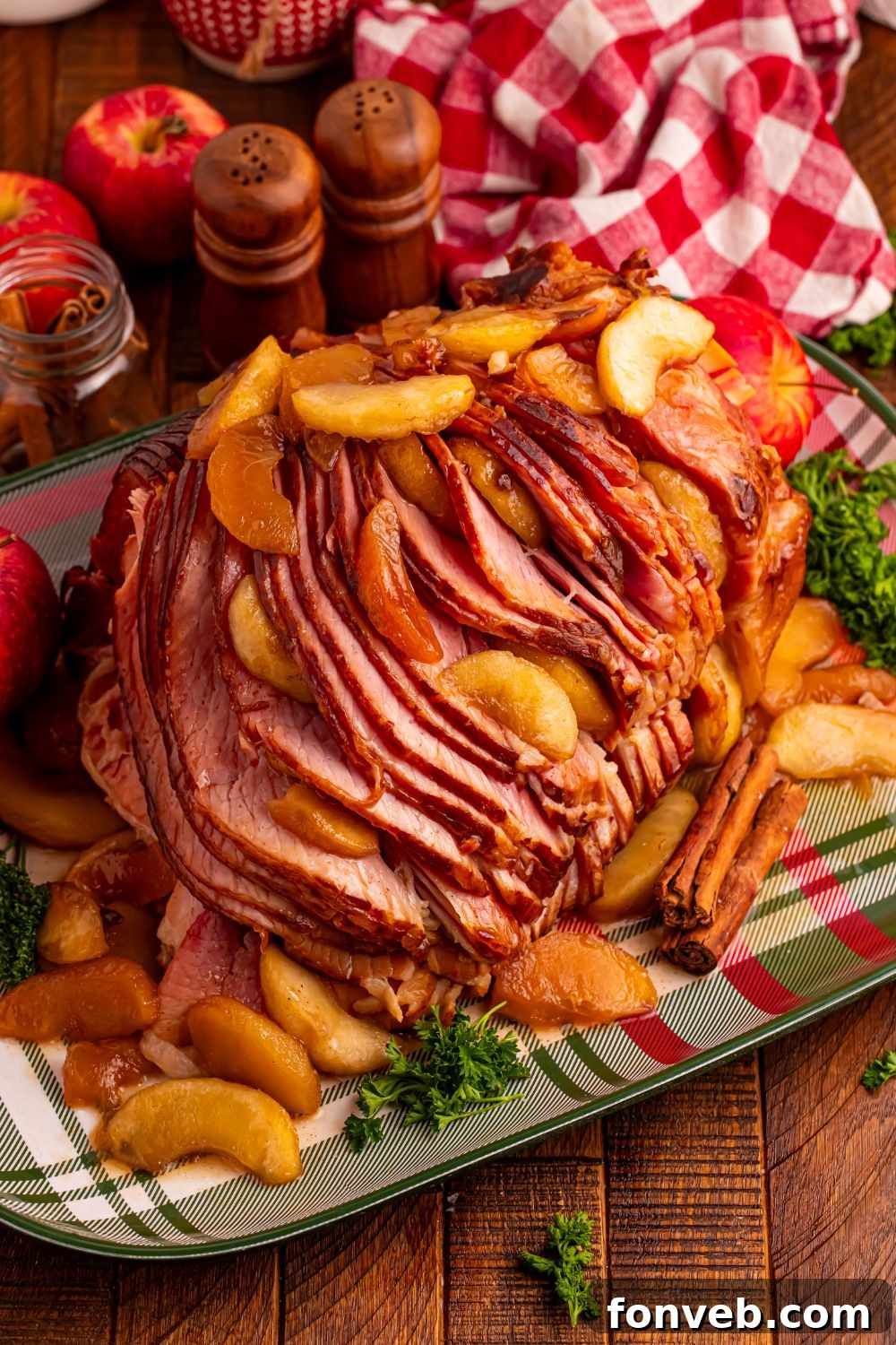Tender and Juicy Slow Cooker Apple Glazed Ham 4 A plaid platter on a wooden table with a large Slow Cooker Apple Glazed Ham on platter, and fall themed items around it