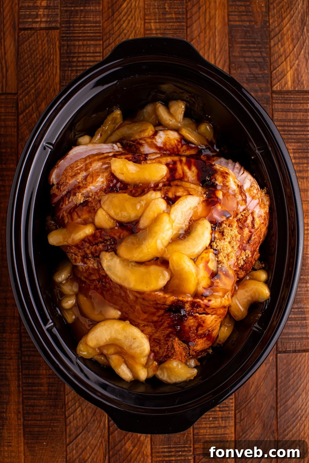 Tender and Juicy Slow Cooker Apple Glazed Ham 7 wooden table with a black crockpot in center with a sliced ham topped with spiced apples