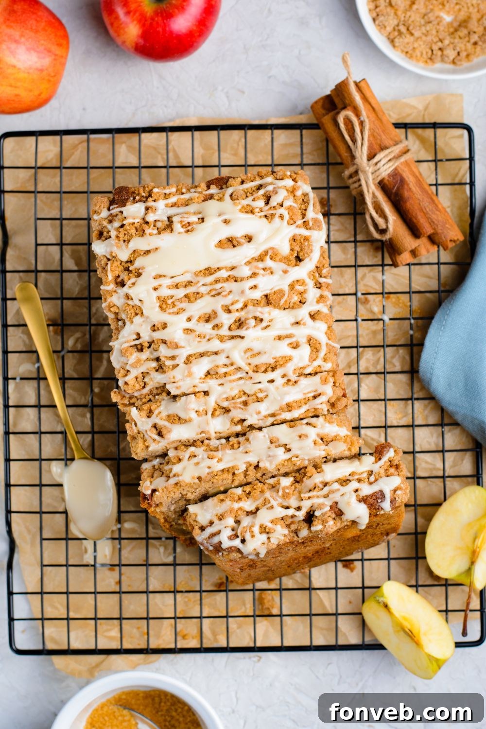 Quick Glazed Apple Cinnamon Loaf 16 A freshly baked Apple Cinnamon Loaf Cake, beautifully glazed and resting on a wire cooling rack on a marble counter, surrounded by decorative cinnamon sticks, whole apples, and sliced apples, capturing the essence of fall baking.