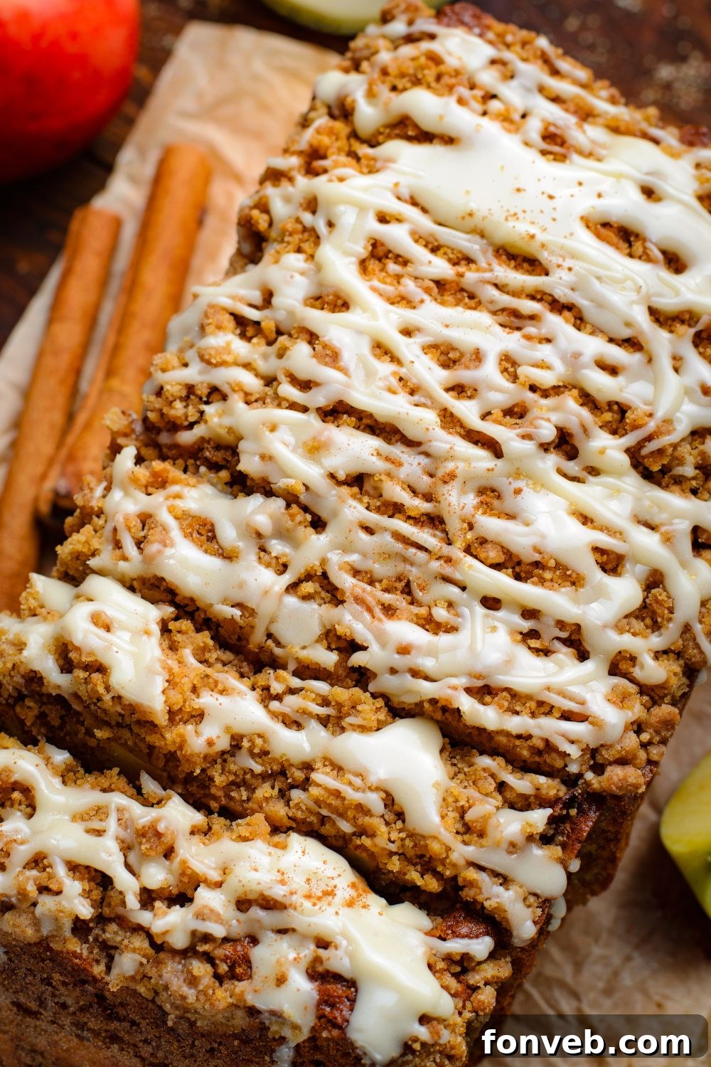 Quick Glazed Apple Cinnamon Loaf 20 An Apple Cinnamon Loaf Cake, beautifully turned to its side, showcasing its thick, inviting slices on a wooden table, accented by cinnamon sticks and a vibrant red apple in the background, creating a cozy autumn display.