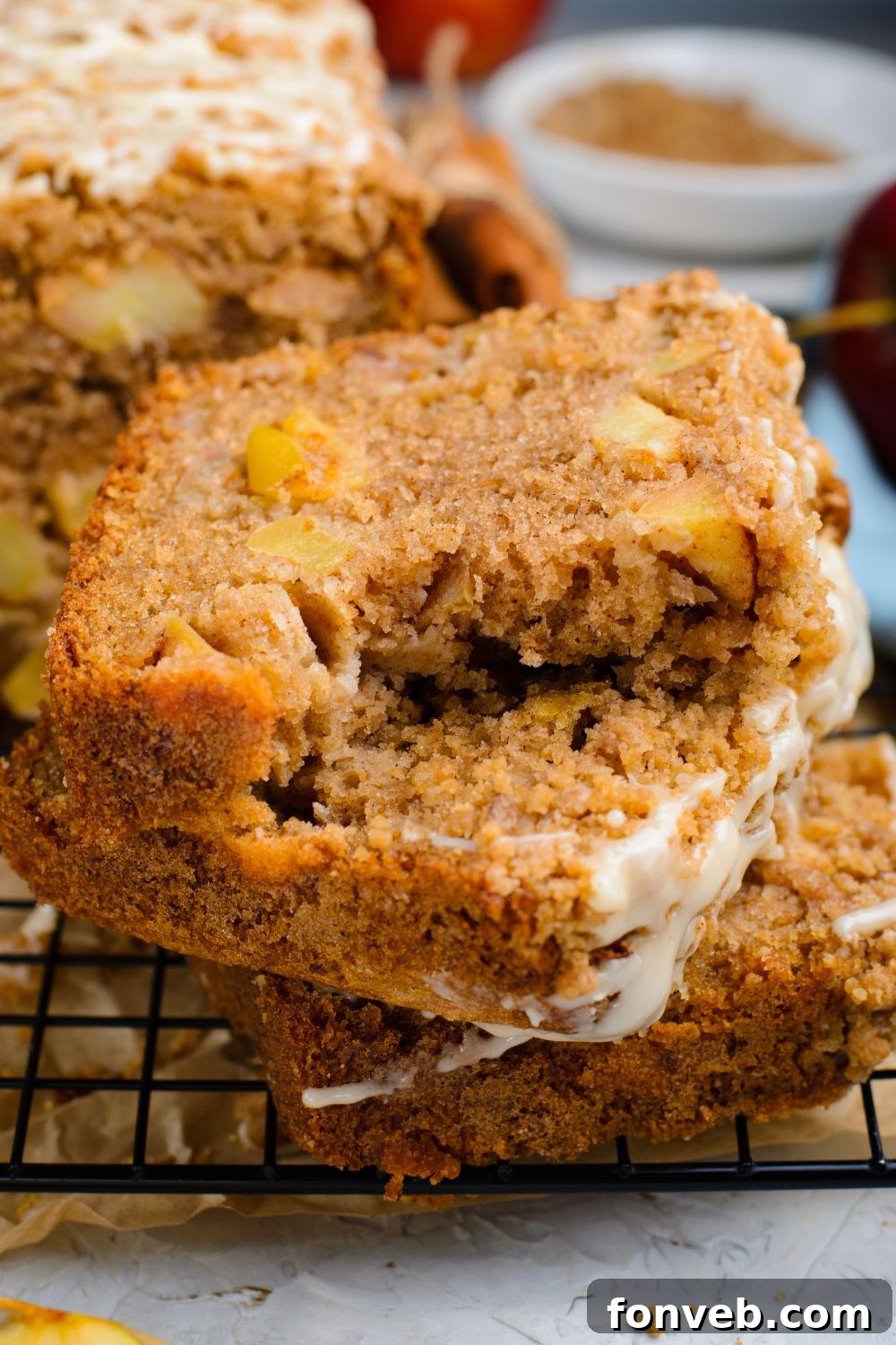 Quick Glazed Apple Cinnamon Loaf 23 Three slices of Apple Cinnamon Loaf Cake, stacked neatly on a wire cooling rack, with a bite taken from the top slice, set against a warm, inviting backdrop.