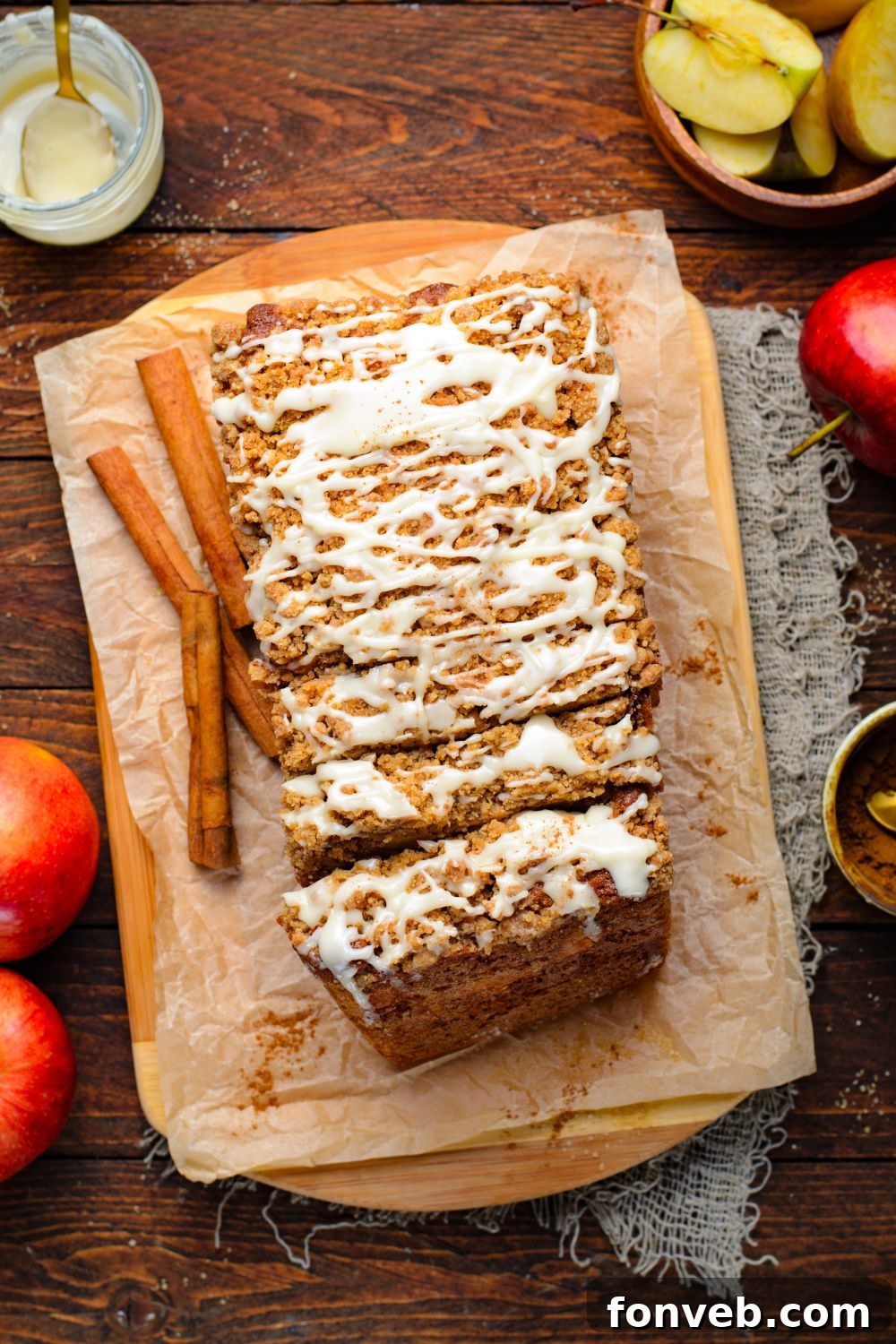 Quick Glazed Apple Cinnamon Loaf 24 A charming overhead view of a wooden table adorned with brown parchment paper, featuring slices of Apple Cinnamon Loaf Cake, with fresh apples and cinnamon sticks artfully arranged around them, creating a rustic and inviting display.