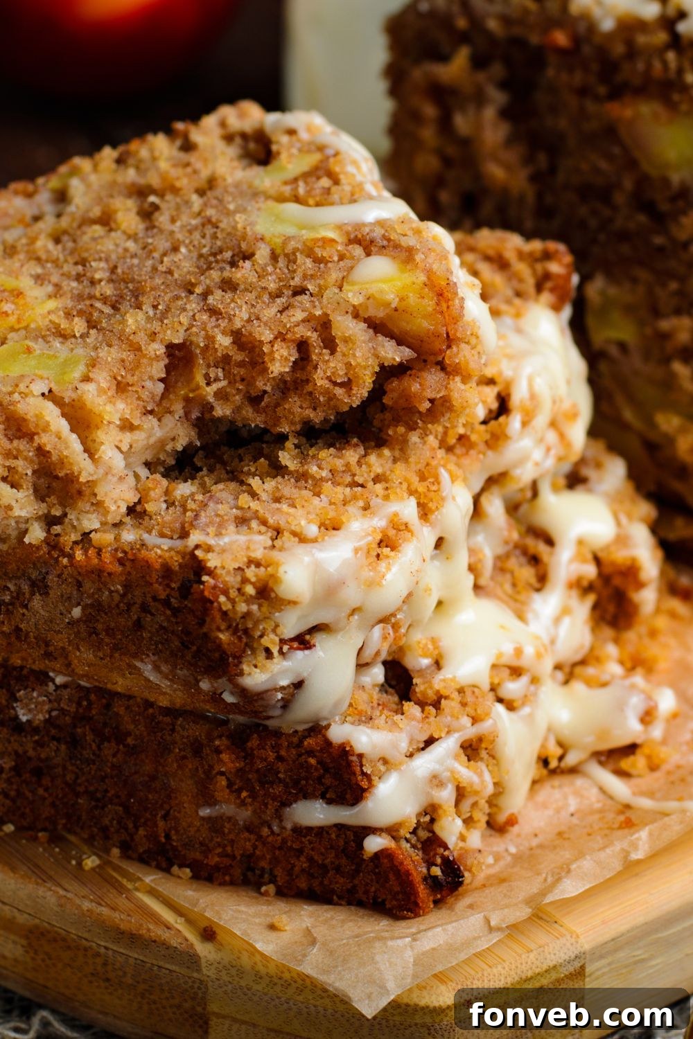Quick Glazed Apple Cinnamon Loaf 27 A few thick slices of Apple Cinnamon Loaf Cake are stacked on a wooden cutting board, with a bite taken from the top slice, creating an inviting and rustic presentation.