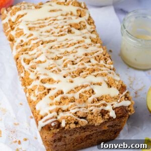 Quick Glazed Apple Cinnamon Loaf 31 A freshly baked Apple Cinnamon Loaf Cake, drizzled with white glaze, resting on a wooden table alongside a jar of extra glaze and fresh apples, evoking a warm autumn scene.